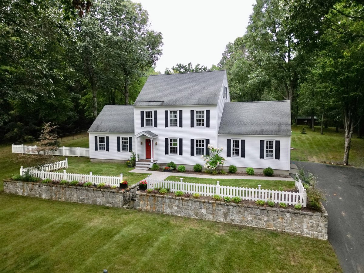 Front elevation drone aerial showcasing colonial home, stone wall, and landscaped grounds